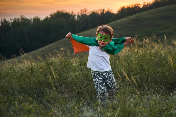 Liten pojke spelar en superhjälte. Kid i en superheros kostym. Happy Child springer för att träffa fotografen. — Stockfoto