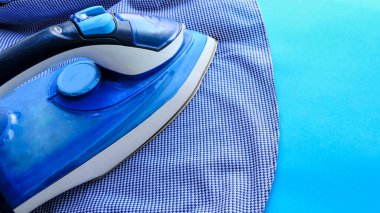 Pembe arka plandaki ütü masasında elektrikli ütü ve gömlek. Demir mavisi çizgili gömlek.