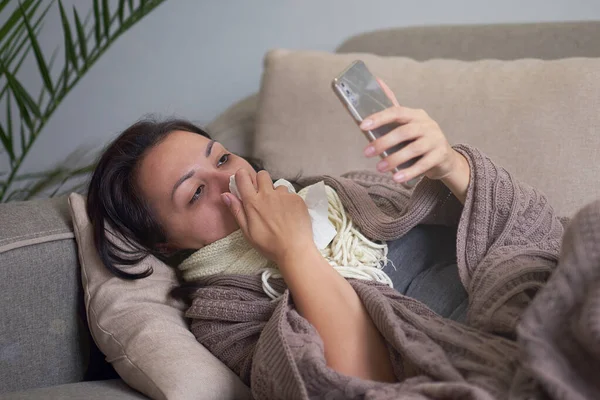 Ill boos vrouw blazen neus kreeg griep gevangen koude niezen in weefsel zitten op de bank, zieke meisjespijn keel, grijs met een sjaal keel en drinkt aspirine thuis, hooikoorts concept — Stockfoto