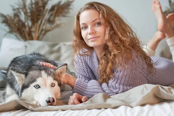 Женщина в уютном трикотажном свитере расслабляется на кровати. Ее собака рядом. Лучшие друзья концепция — стоковое фото