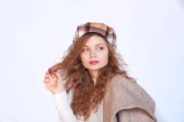 Beyaz bir arka planda Fransız tarzı giyinmiş güzel bir kız. Kızıl saçlı kadın bir paltoya sarılı, kışlık giysiler. Sıcak kıyafetler içinde gülümseyen kadın, kış portresi.