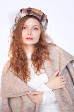 Beyaz bir arka planda Fransız tarzı giyinmiş güzel bir kız. Kızıl saçlı kadın bir paltoya sarılı, kışlık giysiler. Sıcak kıyafetler içinde gülümseyen kadın, kış portresi.