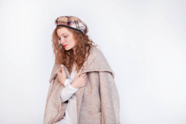 Beyaz bir arka planda Fransız tarzı giyinmiş güzel bir kız. Kızıl saçlı kadın bir paltoya sarılı, kışlık giysiler. Sıcak kıyafetler içinde gülümseyen kadın, kış portresi.