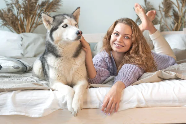 Девочка в спальне лежит на кровати и обнимает собаку. — стоковое фото