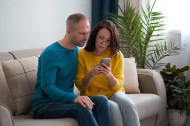 Çekici genç evli bir çift oturma odasındaki kanepede oturuyor ve akıllı telefon cihazından bir şey izliyorlar. Kapalı.