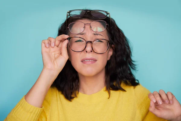 frames trying many eyeglasses. girl holding glasses standing on turquoise background, Concept: poor eyesight.