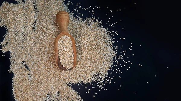 Białe nasiona quinoa na czarnym tle. Quinoa w łyżce na stole kuchennym widok z góry. Zdrowe i dietetyczne produkty Superfood. — Zdjęcie stockowe