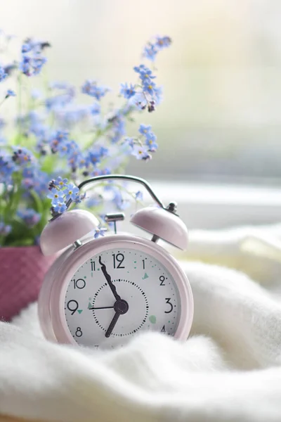 Buquê primavera de flores e uma xadrez branco acolhedor no peitoril da janela. relógio rosa pela janela mostra hora da manhã — Fotografia de Stock