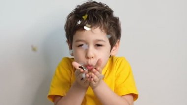 Doğum günün kutlu olsun çocuğum. Çekici, sevimli, sevimli küçük çocuğun sana konfeti üflerken ki fotoğrafı. Duygusal yüz ifadesiyle bayram havasını göstermek için. Stok görüntüleri. Slow Motion videosu. Kapat.