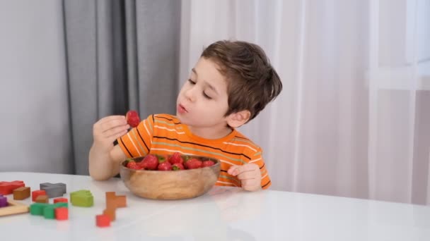 朝食時の笑顔の男の子果物のイチゴを食べる。ストック映像だ。スローモーションビデオ。閉じろ! — ストック動画