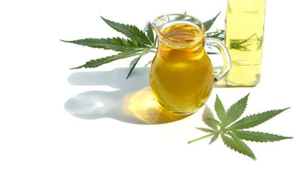 Semillas de cáñamo sobre la mesa, aceite en un frasco de vidrio, hojas de cannabis aisladas sobre fondo blanco — Foto de Stock