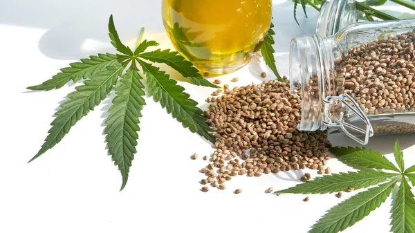 桌上的种子大麻，玻璃瓶里的油，白色背景下的大麻叶 — 图库照片