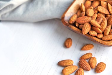 Beyaz ahşap bir masada, tahtadan bir kasede fındık.