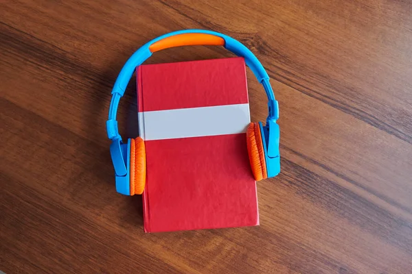 Concepto de audio libro. Auriculares y libro rojo en una mesa de madera. Vista superior con espacio para su texto. Plano, vista superior, espacio para copiar — Foto de Stock