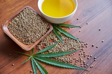 Masadaki kenevir tohumları, cam kavanozdaki yağ, beyaz arka plandaki kenevir yaprakları.