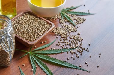 Masadaki kenevir tohumları, cam kavanozdaki yağ, beyaz arka plandaki kenevir yaprakları.