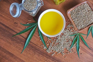 Masadaki kenevir tohumları, cam kavanozdaki yağ, beyaz arka plandaki kenevir yaprakları.