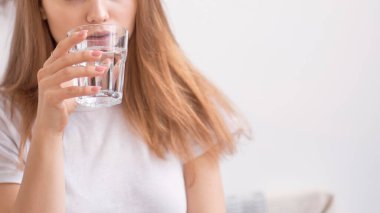 Tanınmayacak kadar güzel bir genç kız camdan su içiyor. Su içen genç ve mutlu bir kadın. Elinde şeffaf camlar tutan gülümseyen beyaz kadın model. Yakın çekim..