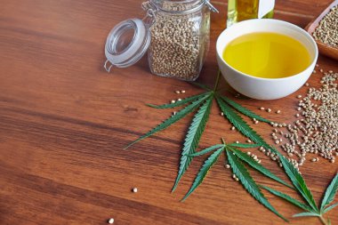 Masadaki kenevir tohumları, cam kavanozdaki yağ, beyaz arka plandaki kenevir yaprakları.