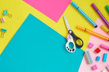 Okul malzemeleri, sarı arka planda kırtasiye malzemesi - manşet için yer. Çocuk kalemle çizmeye ve renkli kağıt uygulamaya hazır. Üst görünüm.