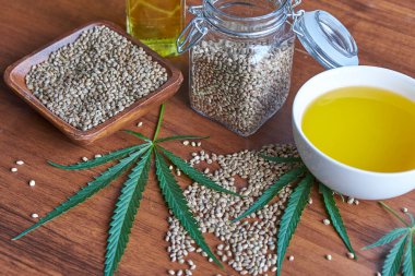 Masadaki kenevir tohumları, cam kavanozdaki yağ, beyaz arka plandaki kenevir yaprakları.