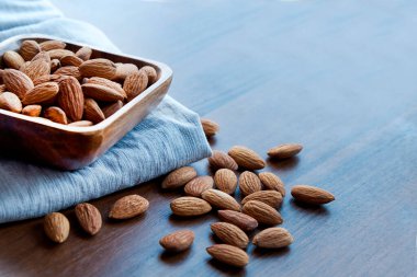 Bademler küçük ahşap kasede. Bademler karanlık masaya serilmişti. Badem fıstıklı kaseler, üst manzara. Soyulmuş badem deseni