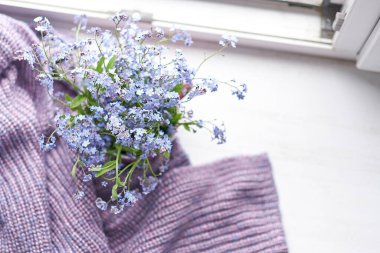 Ahşap bankta mor, sıcak ekose battaniye. Fotoğraf tonlu, seçici odaklanma. Samimi ev hayatı: Bahar çiçekleri, pencere kenarında sıcak ekoseli.