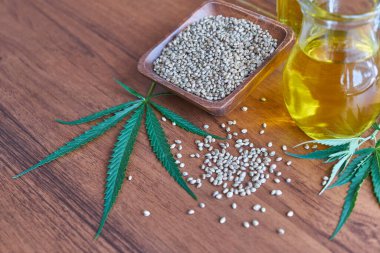 Masadaki kenevir tohumları, cam kavanozdaki yağ, beyaz arka plandaki kenevir yaprakları.