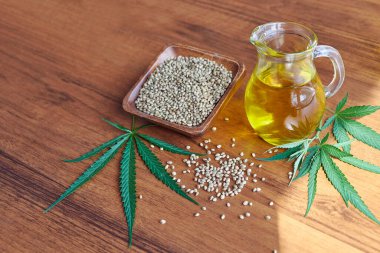 Masadaki kenevir tohumları, cam kavanozdaki yağ, beyaz arka plandaki kenevir yaprakları.