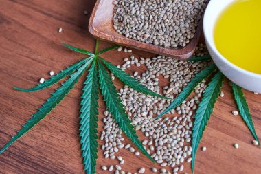 Masadaki kenevir tohumları, cam kavanozdaki yağ, beyaz arka plandaki kenevir yaprakları.