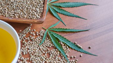 Masadaki kenevir tohumları, cam kavanozdaki yağ, beyaz arka plandaki kenevir yaprakları.