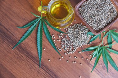 Masadaki kenevir tohumları, cam kavanozdaki yağ, beyaz arka plandaki kenevir yaprakları.