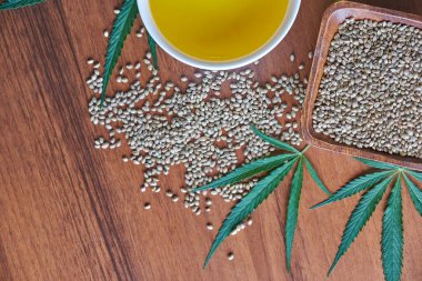 Masadaki kenevir tohumları, cam kavanozdaki yağ, beyaz arka plandaki kenevir yaprakları.