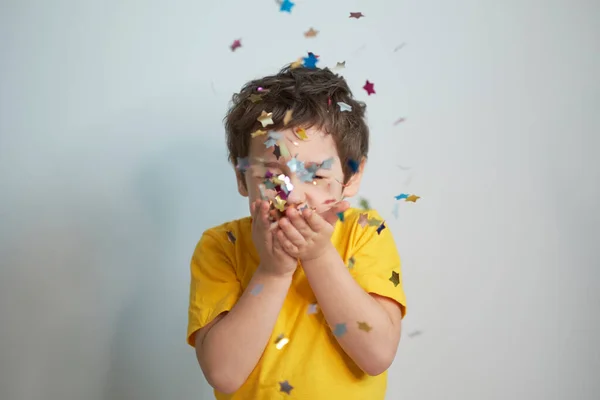 Grattis på födelsedagen. Foto av charmig söt fascinerande trevlig liten pojke blåser konfetti på dig för att visa hennes festliga humör med känslomässiga ansiktsuttryck. — Stockfoto