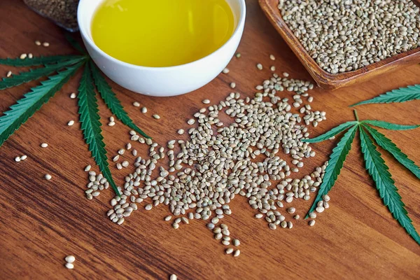 Masadaki kenevir tohumları, cam kavanozdaki yağ, beyaz arka plandaki kenevir yaprakları.