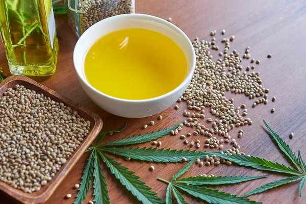 Masadaki kenevir tohumları, cam kavanozdaki yağ, beyaz arka plandaki kenevir yaprakları.