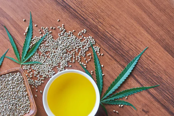 Masadaki kenevir tohumları, cam kavanozdaki yağ, beyaz arka plandaki kenevir yaprakları.