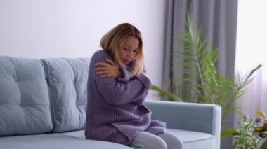 Asyalı kadın evde sıcak örülmüş süvetere sarılmaya çalışıyor. Soğuk mevsim. Stok görüntüleri. Kapat..