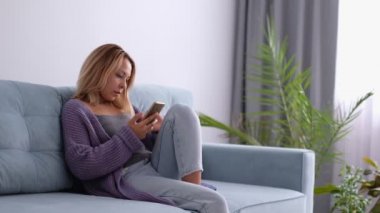 Yakından bakınca Asyalı kaygısız genç kadın kanepeye yaslanıyor akıllı telefon konuşmaları yapıyor internette sörf yapıyor, boş zaman kavramı.