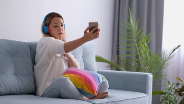 Time lapse av vackra kvinna meddelanden på smartphone, läsa bok, chatta på telefon, och lyssna på musik med hörlurar medan spendera dagen på soffan — Stockvideo