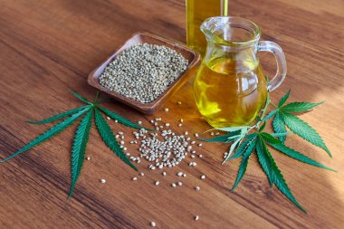Masadaki kenevir tohumları, cam kavanozdaki yağ, beyaz arka plandaki kenevir yaprakları.