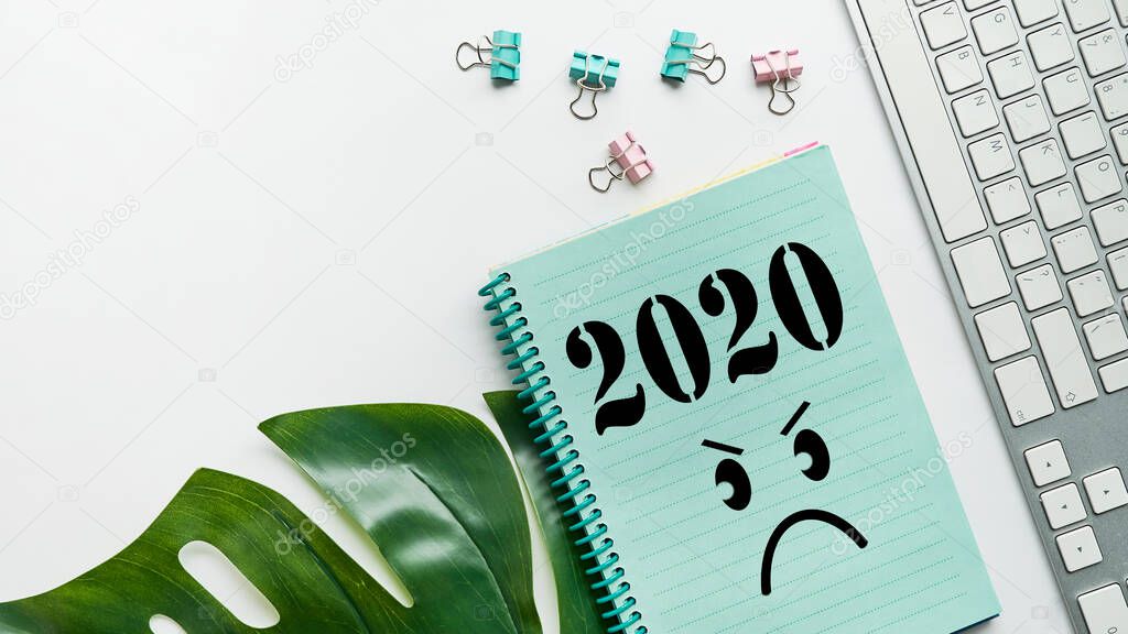 desk with notepad with round sad emoji-the concept of a sad year. 2020 and a sad face. 2020 horrible year concept. Close up.