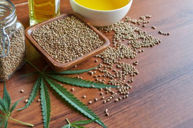 Masadaki kenevir tohumları, cam kavanozdaki yağ, beyaz arka plandaki kenevir yaprakları.