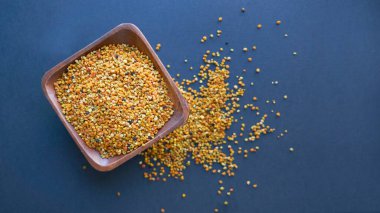 Tahta kaşıkta polen, sağlıklı besin maddeleri. Siyah bir arkaplana yaklaş. Üst manzara, düz yatış. metin için boşluk kopyala.