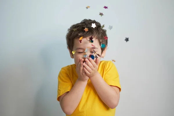 Grattis på födelsedagen. Foto av charmig söt fascinerande trevlig liten pojke blåser konfetti på dig för att visa hennes festliga humör med känslomässiga ansiktsuttryck. — Stockfoto