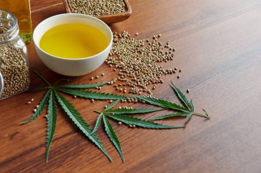 Masadaki kenevir tohumları, cam kavanozdaki yağ, beyaz arka plandaki kenevir yaprakları.