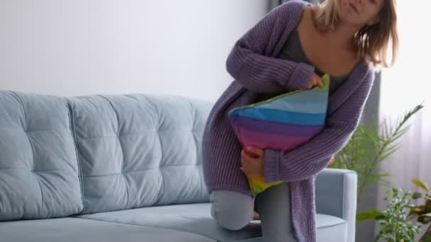 Kobieta w miękkim ciepłym swetrze z dzianiny siada na kanapie i przytula poduszkę, nudzi się sama w domu — Wideo stockowe