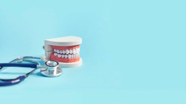 Mavi arka planda steteskobu olan beyaz dişli bir model. Diş sağlığıma. Dişçi günü konsepti. metin için boşluk kopyala.