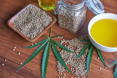 Masadaki kenevir tohumları, cam kavanozdaki yağ, beyaz arka plandaki kenevir yaprakları.