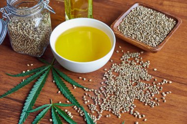 Masadaki kenevir tohumları, cam kavanozdaki yağ, beyaz arka plandaki kenevir yaprakları.